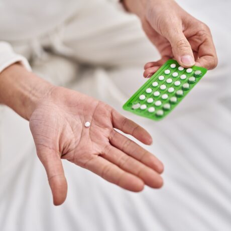 Detaliu cu mână de femeie care ține o pilulă, sugestiv pentru terapia de substituție hormonală