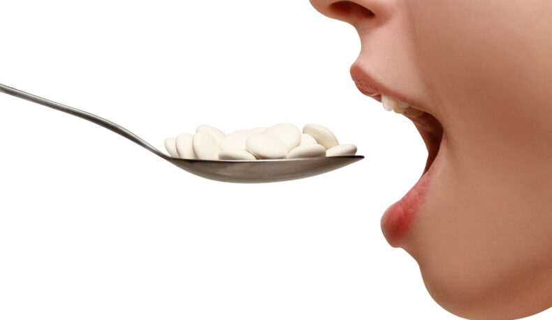 Detaliu cu gură și o lingură cu pastile albe, sugestiv pentru excesul de vitamina D