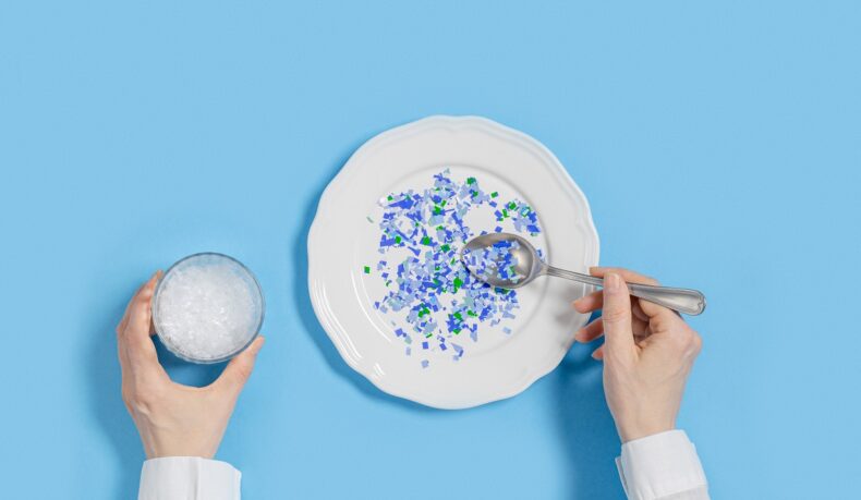 Detaliu cu persoană care mănâncă dintr-o farfurie cu bucăți mici de plastic colorat și ține un pahar cu plastic în interior, sugestiv petru alimentele care conțin cel mai mult plastic