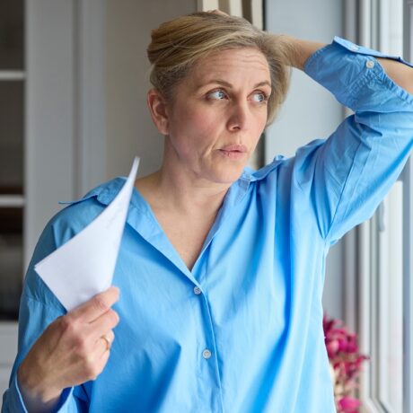 Femeie cu bufeuri care își face aer cu o hârtie, sugestiv pentru simptomele de menopauză