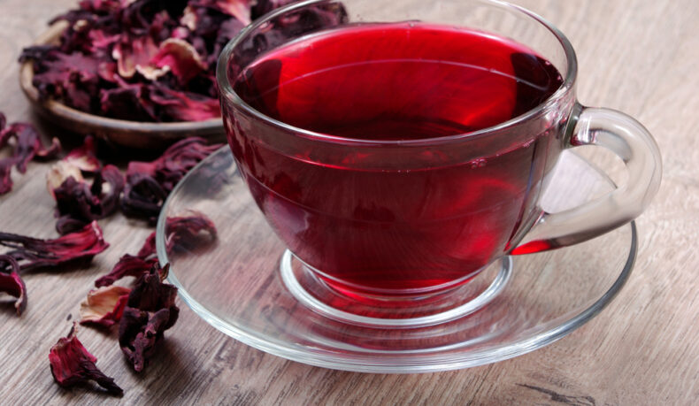 O ceașcă cu ceai de hibiscus, lângă petale uscate de hibiscus