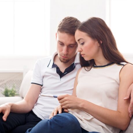 Cuplu trist care se uită la un test de sarcină în mâna femeii, sugestiv pentru infertilitate