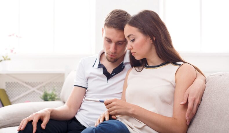 Cuplu trist care se uită la un test de sarcină în mâna femeii, sugestiv pentru infertilitate