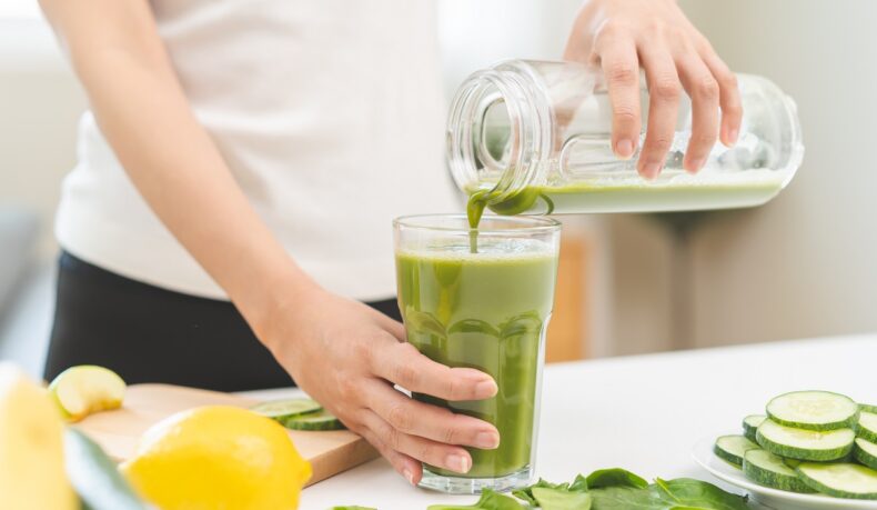 Detaliu cu o fată care toarnă în pahar un suc verde de legume, una dintre soluțiile recomandate pentru detoxifierea colonului