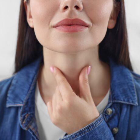 Femeie care își palpează gâtul, sugestiv pentru o boală autoimună a tiroidei