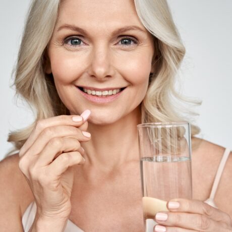 Femeie de vârstă mijlocie care ia o pastilă cu un pahar cu apă, sugestiv pentru vitamine și minerale pentru femei la menopauză