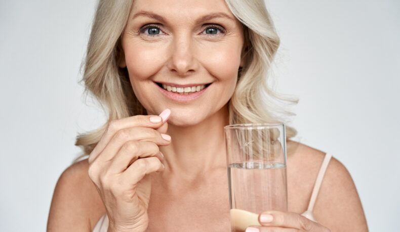 Femeie de vârstă mijlocie care ia o pastilă cu un pahar cu apă, sugestiv pentru vitamine și minerale pentru femei la menopauză