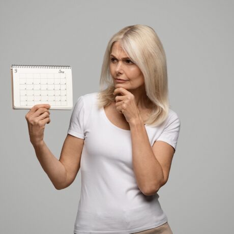 Femeie gânditoare care ține un calendar gol în mână, sugestiv pentru dereglările ciclului menstrual ce caracterizează perimenopauza