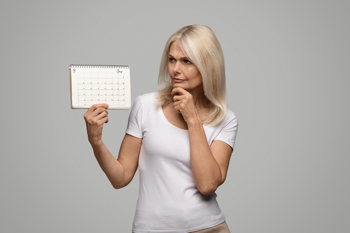 Femeie gânditoare care ține un calendar gol în mână, sugestiv pentru dereglările ciclului menstrual ce caracterizează perimenopauza