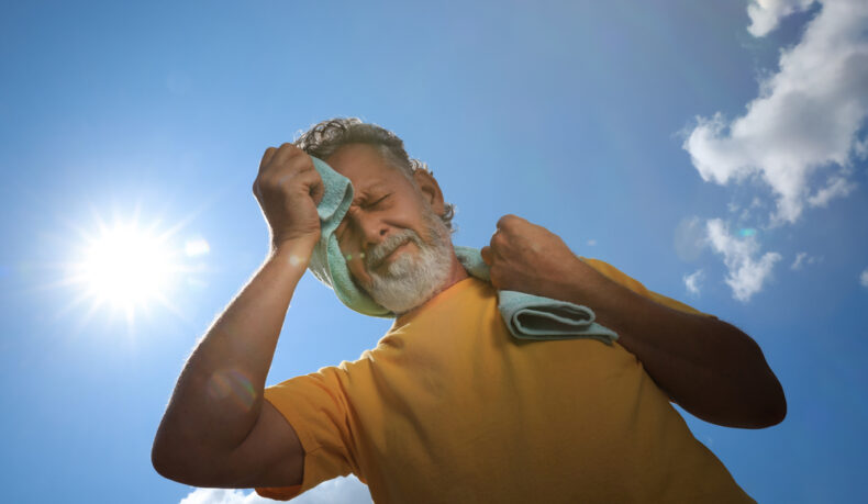 Un bărbat în vârstă care ține un prosop pe frunte și umeri, în lumina soarelui