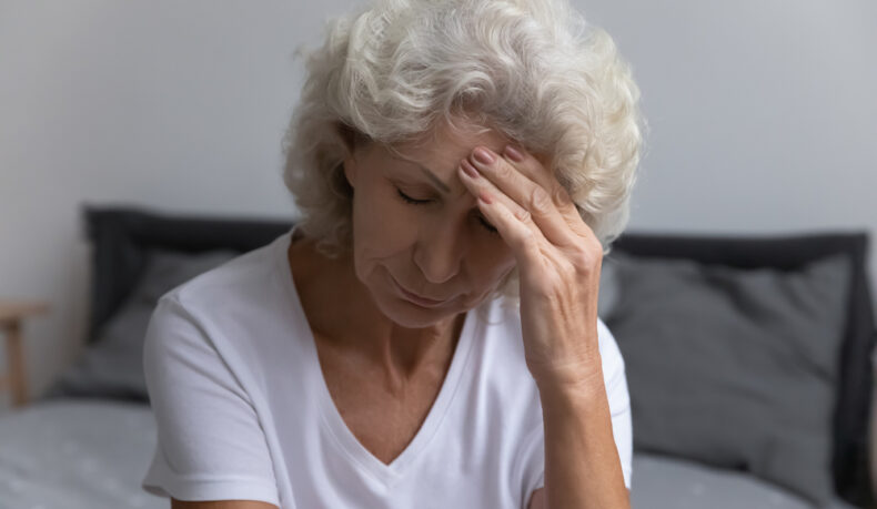 O femeie în vârstă care își ține mâna pe frunte din cauza senzației de oboseală