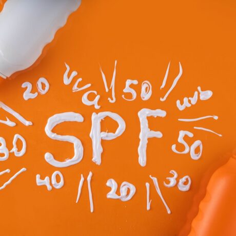 Sticle de plastic cu cremă de plajă, alături de cuvântul SPF scris cu cremă albă pe fundal portocaliu: SPF 50, 40, 30, 20