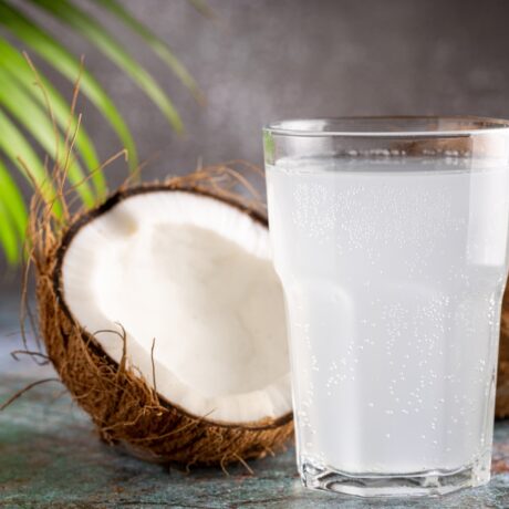 Un pahar cu apă de nucă de cocos, lângă două nuci de cocos