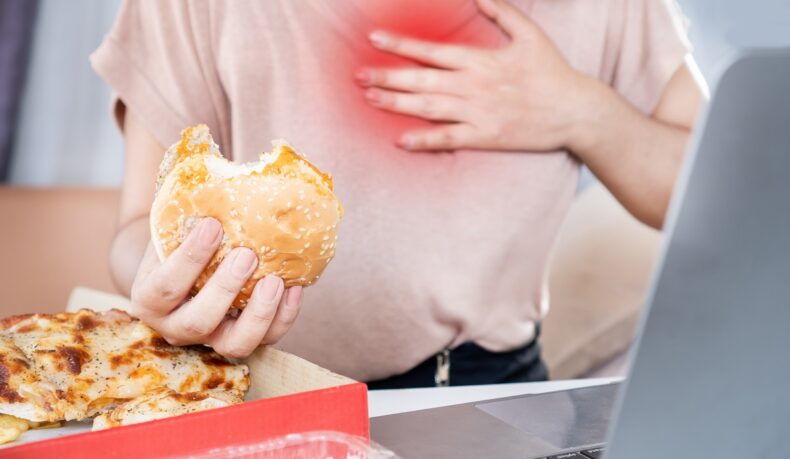 O femeie cu arsuri gastrice care mănâncă burger și pizza, alimente care provoacă reflux gastroesofagian