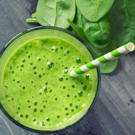 Un pahar cu smoothie verde, lângă frunze de spanac