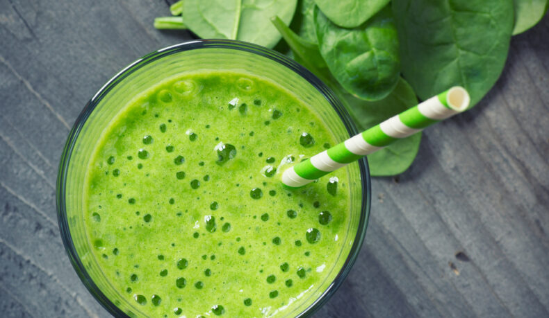 Un pahar cu smoothie verde, lângă frunze de spanac