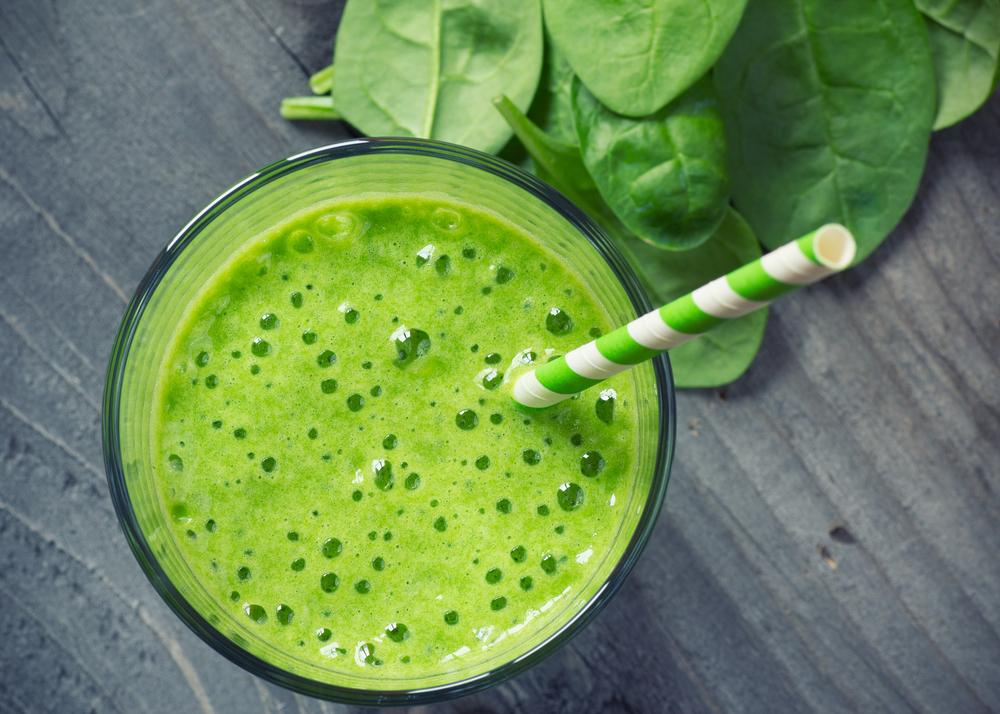 Un pahar cu smoothie verde, lângă frunze de spanac