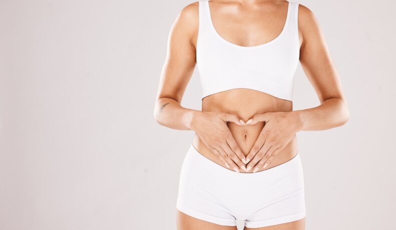 O femeie care își ține mâinile în formă de inimă pe abdomen, sugestiv pentru microbiomul intestinal și sănătatea pielii