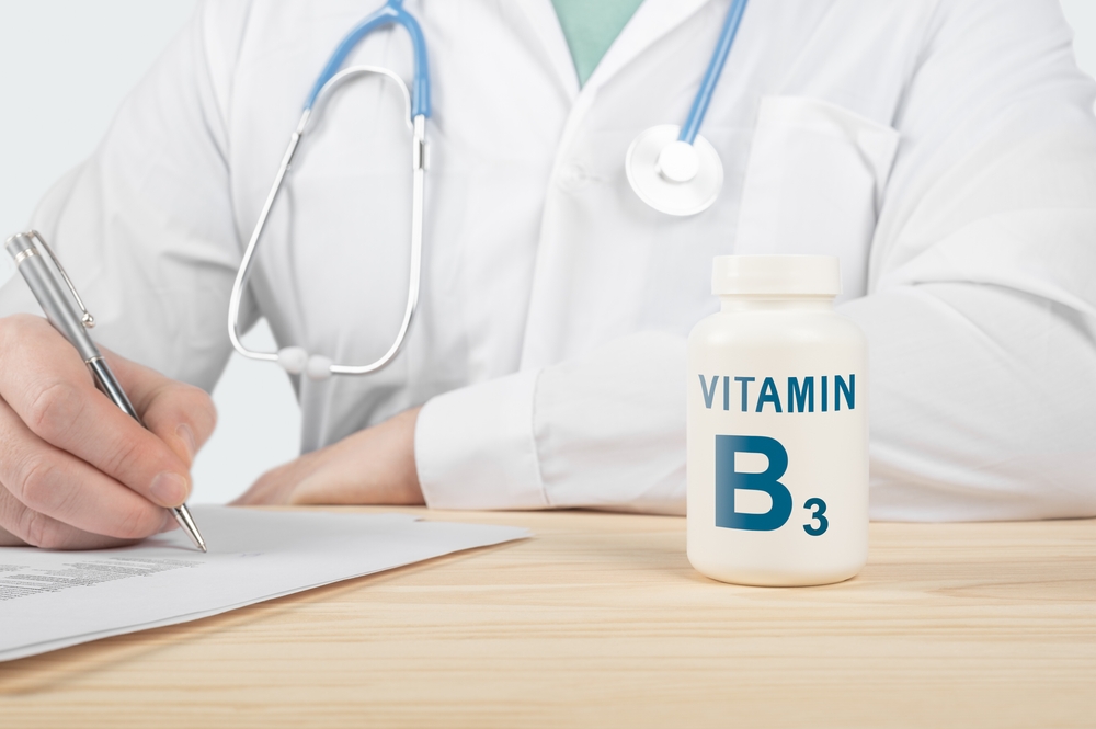 Un medic care scrie pe hârtie, lângă un borcan pe care scrie vitamina B3