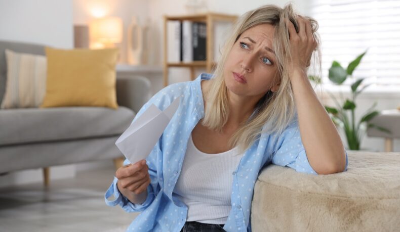 o femeie tristă care își face aer cu o hârtie, sugestiv pentru bufeurile de la menopauză