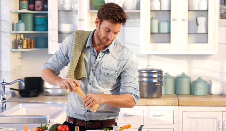 barbat care gateste in bucatarie si tine in maini o rasnita de piper