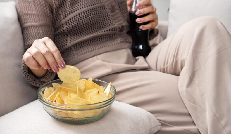 O femeie care mananca chipsuri si bea cola